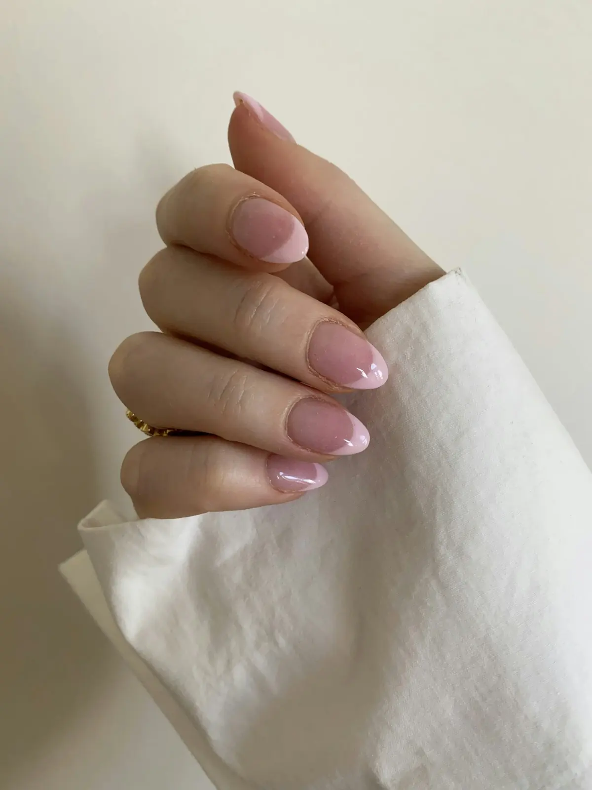 French manucure rosée sur ongles courts, main posée sur un tissu blanc